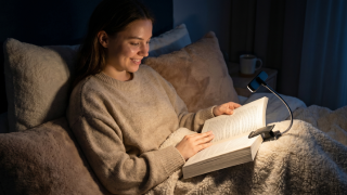 Persona leyendo cómoda en la cama con lámpara de lectura